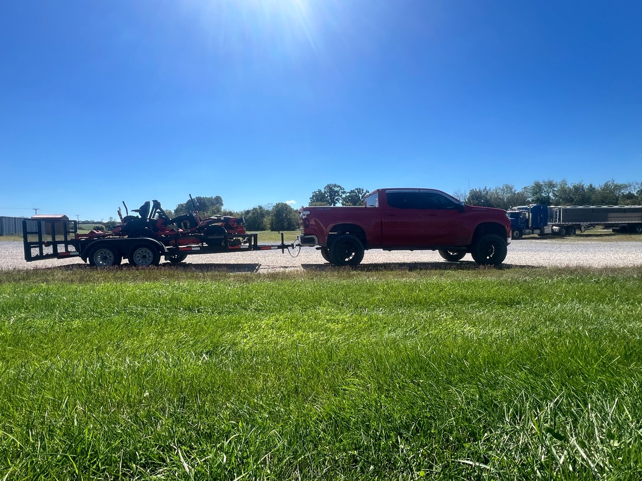 Side profile of a red Chevrolet Silverado and utility trailer loaded with two red zero-turn mowers