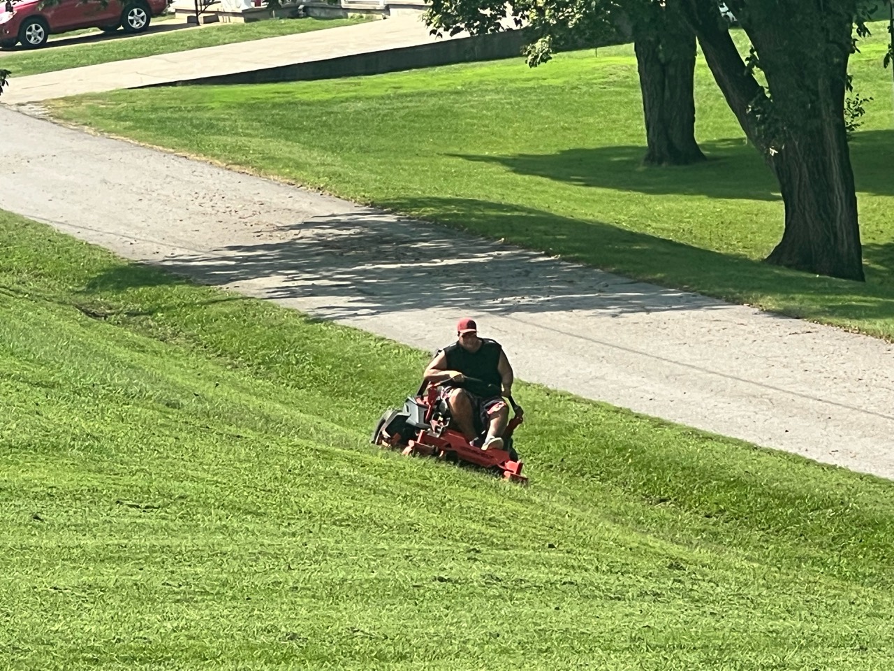 Clay mowing a sloped lawn on a red zero-turn mower