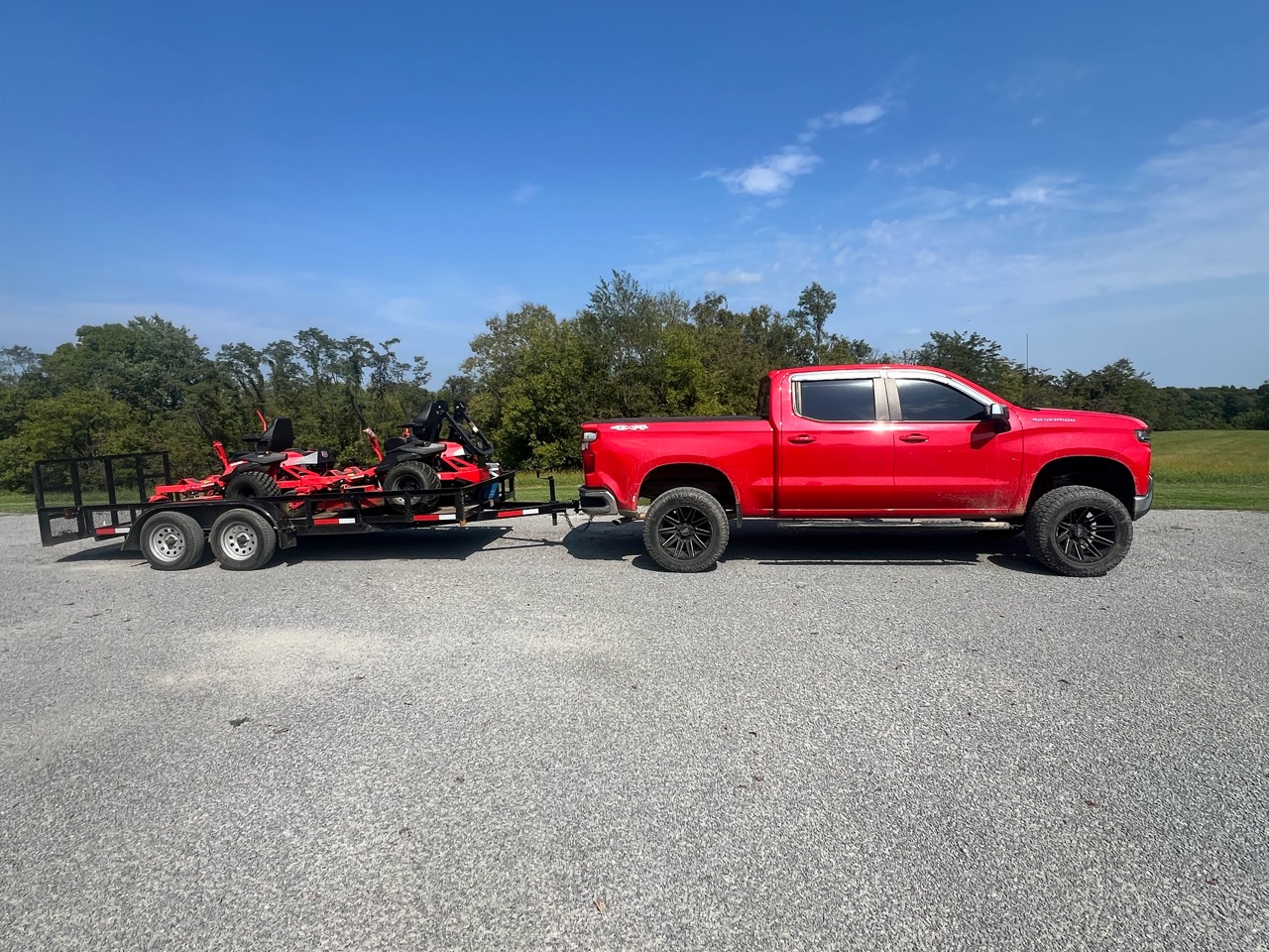 Clay’s red work truck and trailer carrying two red zero-turn mowers